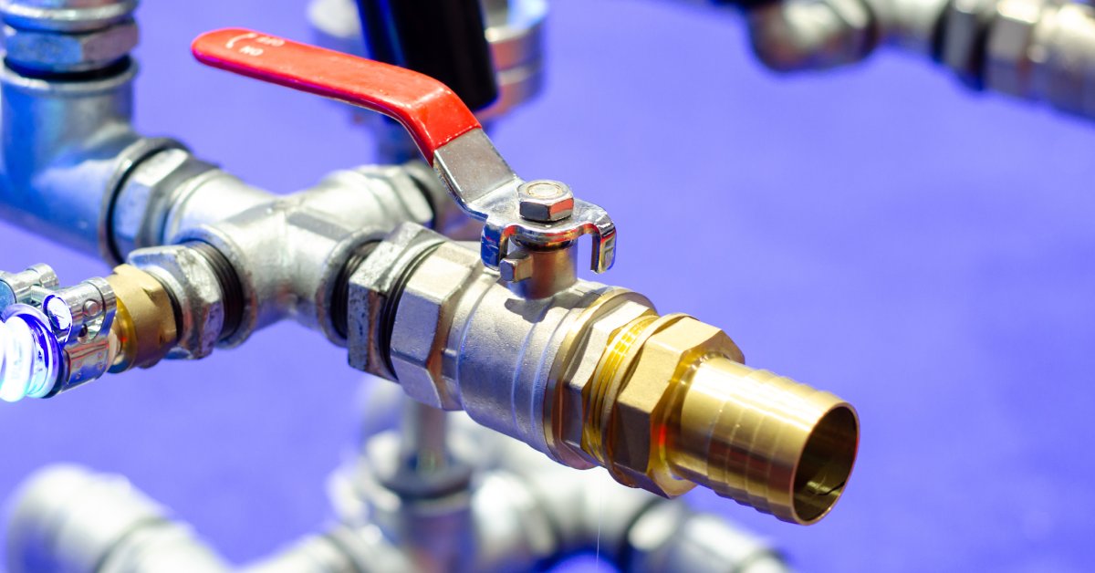 A close-up of metal pipelines with a ball valve. This valve is connected to other pipes in the background.