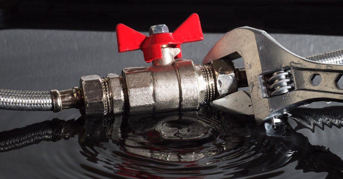 A close-up of a ball valve being adjusted with a wrench that's wet. There's water spilling out the pipe.